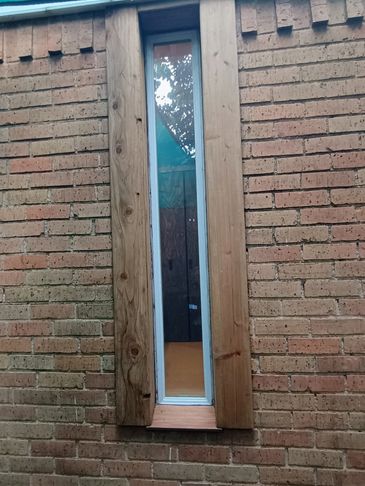 Tall narrow window framed with wood on a brick wall.