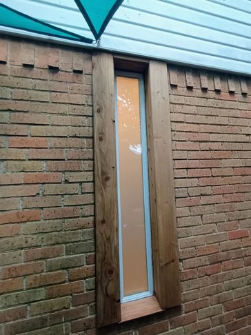 Tall narrow window framed with wood on a brick wall under a blue canopy.