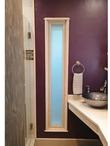 Narrow frosted glass window framed with wood in a purple bathroom wall.