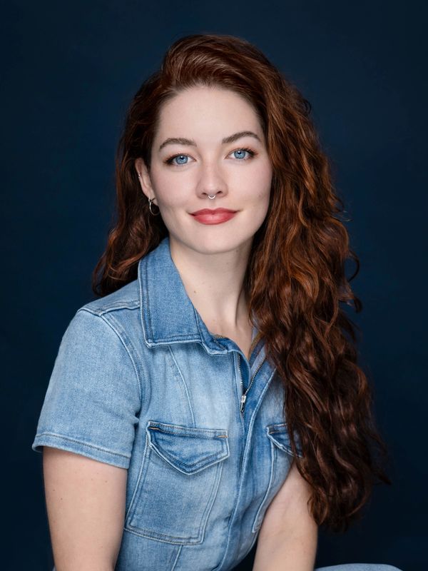 Young woman with long red hair and blue eyes wearing a denim jacket.