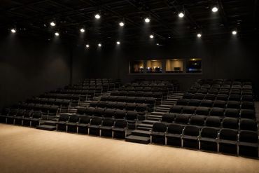 Empty auditorium with rows of black seats and spotlight lighting.