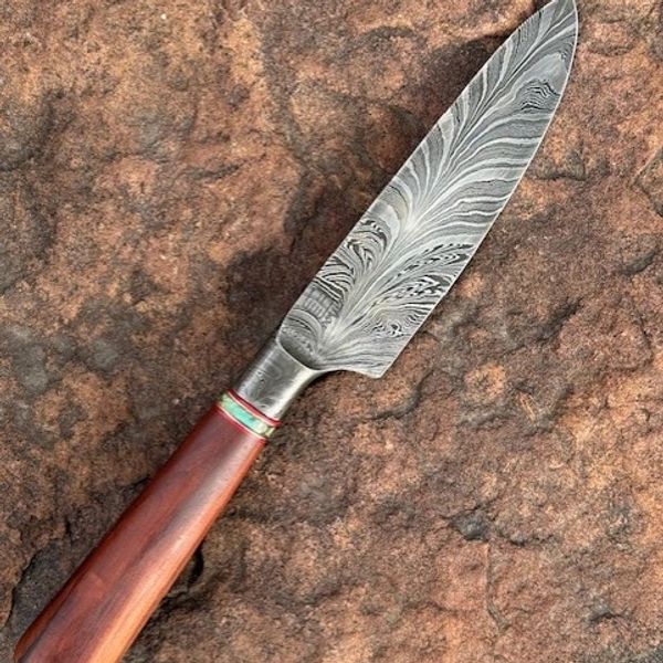 Damascus steel chef's knife with a wooden handle on a textured rock surface.