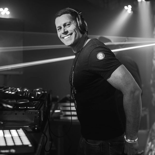 Smiling DJ wearing headphones, performing with equipment in a lively club setting.