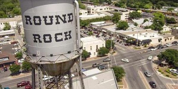 Water tower with 'ROUND ROCK' overlooking a busy urban street.
