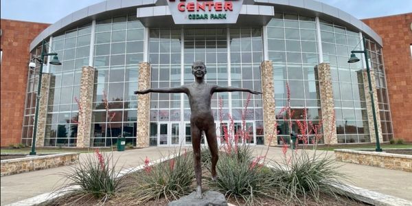 Bronze statue of a boy with arms outstretched in front of a modern glass building.
