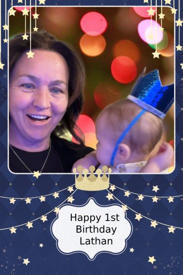 Woman smiling with baby wearing blue crown celebrating 1st birthday.