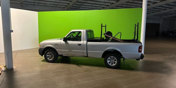 White pickup truck parked indoors with a green screen background.