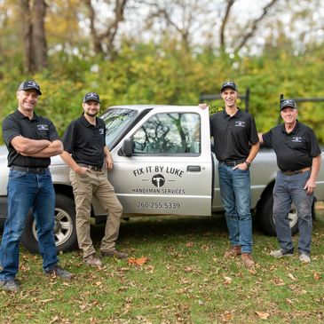 Four men standing in front of a handyman service truck outdoors.