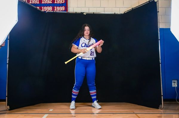Young female softball player posing with bat in uniform.