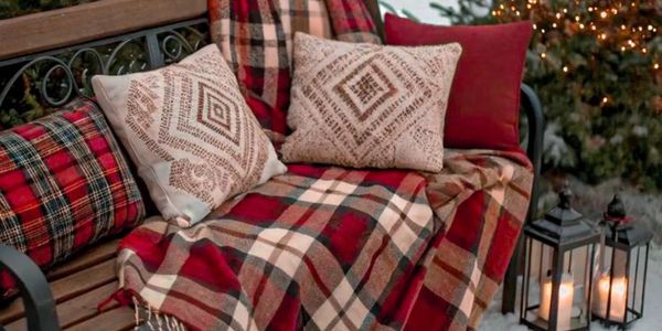 Cozy outdoor bench with cushions and plaid blanket.