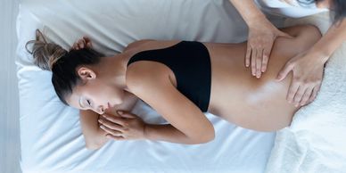 Pregnant woman receiving a relaxing back massage on a white bed.