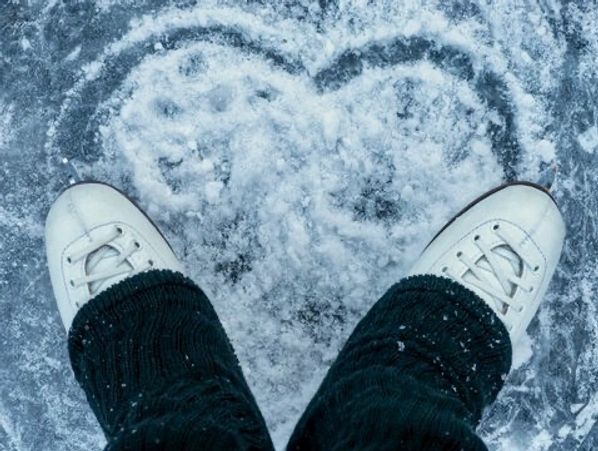 A close-up of ice skates carving a heart-shaped groove into the snowy ice.