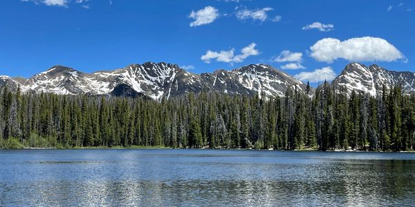 Snow-capped mountains reflect on a serene lake under a clear blue sky.