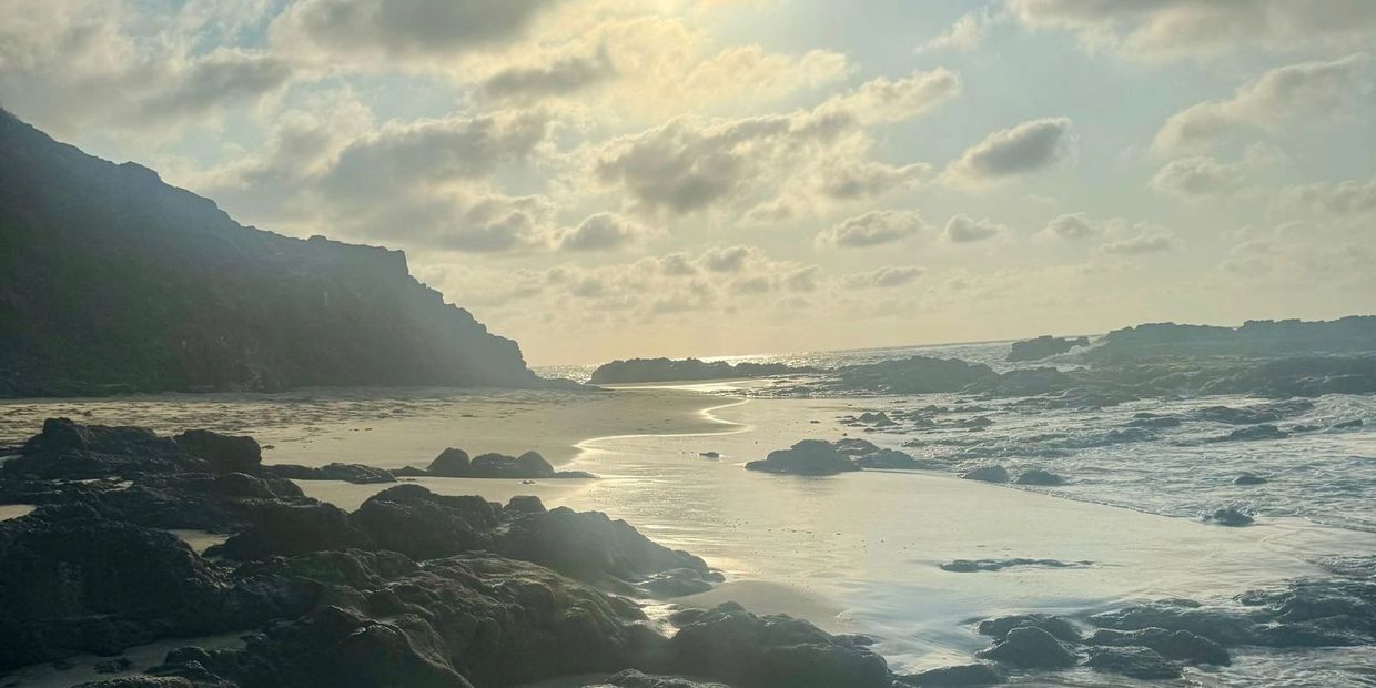 Rocky beach at sunset with cloudy sky.