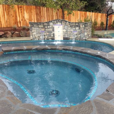 A backyard pool with a stone-accented hot tub and water feature.