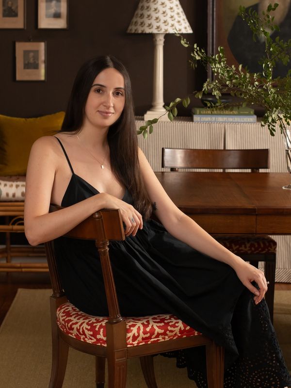 Woman in a black dress sitting on a patterned chair in a warm, elegant room.