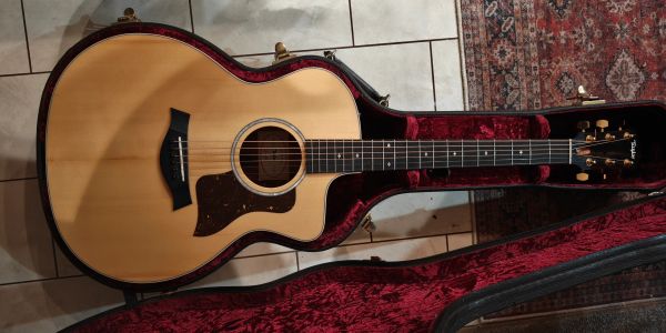 Acoustic guitar resting in a plush-lined case on tiled floor.