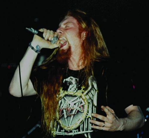Long-haired man passionately singing into a microphone on stage.