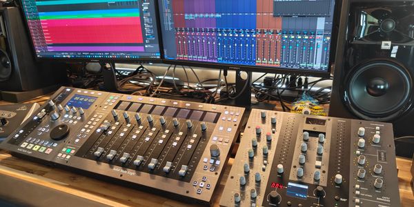 Audio mixing setup with control surfaces and studio monitors.
