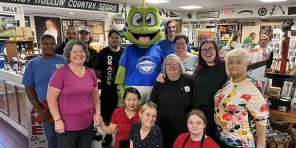 A diverse group of people posing inside a country store with a green mascot.
