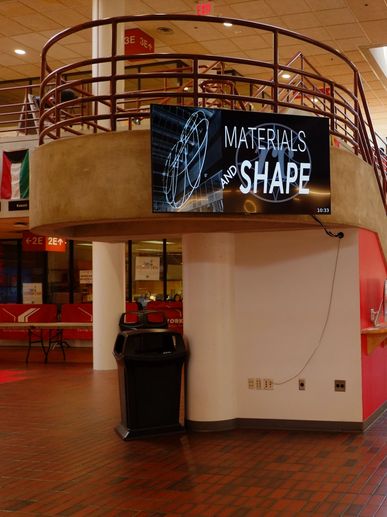 Digital screen displaying 'Materials and Shape' in a modern indoor space.