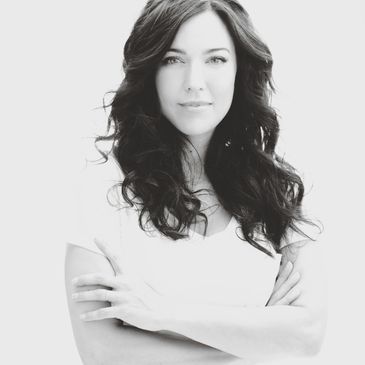 Black and white portrait of a confident woman with long curly hair and arms crossed.
