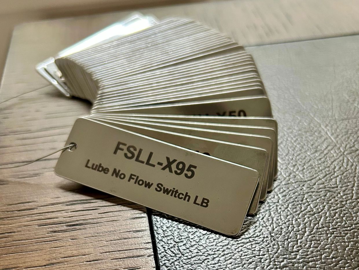 Metal tags labeled with various switch codes, fanned out on a surface.