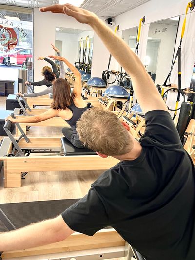 People exercising on Pilates reformer machines in a bright studio.