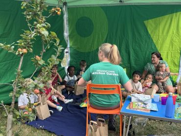 Outdoor storytime with kids and a teacher in a garden.