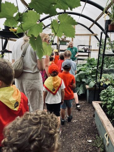Children and adults exploring a greenhouse with plants.