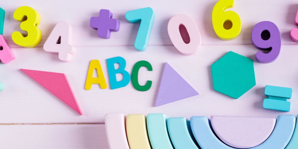 ABC, number and shape blocks pictured up close sitting on a pink wood table. 