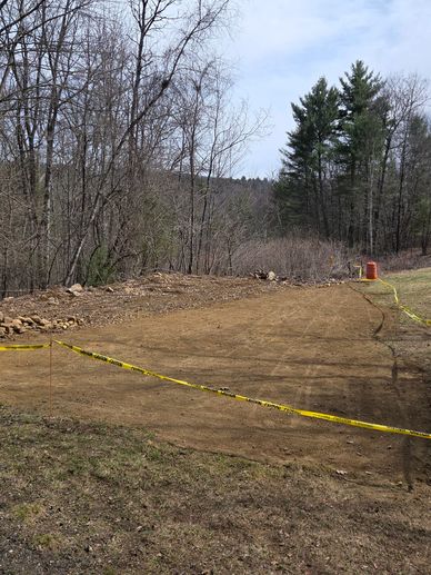 Cleared dirt area bordered by caution tape in a wooded outdoor setting.