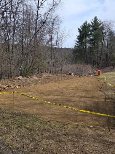 Cleared dirt area bordered by caution tape in a wooded outdoor setting.