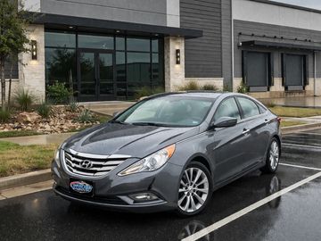 A gray Hyundai sedan parked outside a modern building on a rainy day.