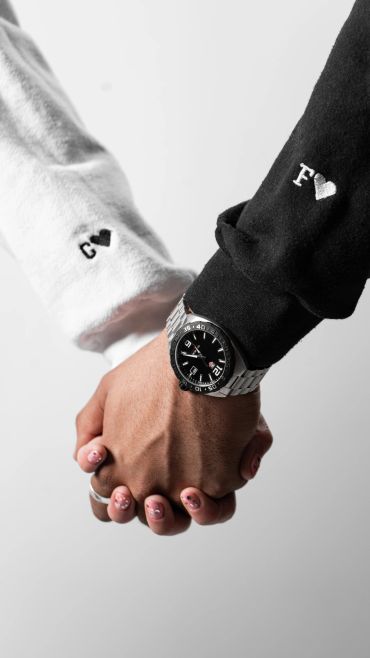 Two people holding hands with embroidered initials on sleeves.