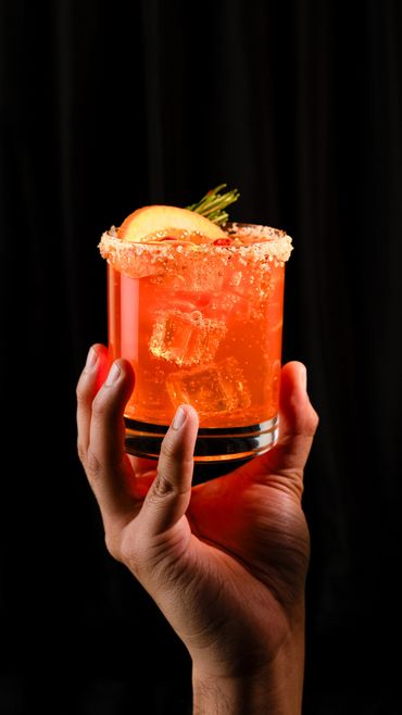 Cóctel Negroni con una cortina negra de fondo, el vaso escarchado con sal rosa, adornado con naranjar