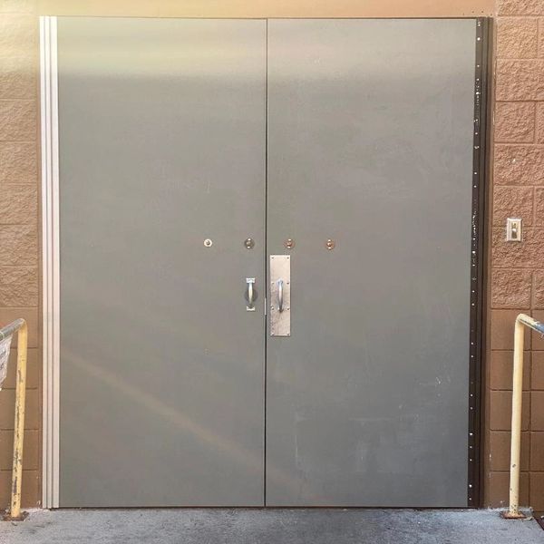 Closed gray double doors on a textured brick wall with metal railings.