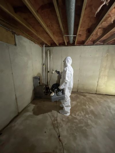 Person in protective suit inspecting a basement corner.