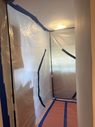 A hallway covered with protective plastic sheeting and blue tape, likely for renovation or painting.