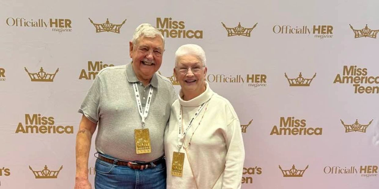 Elderly couple smiling on a red carpet at a Miss America event.