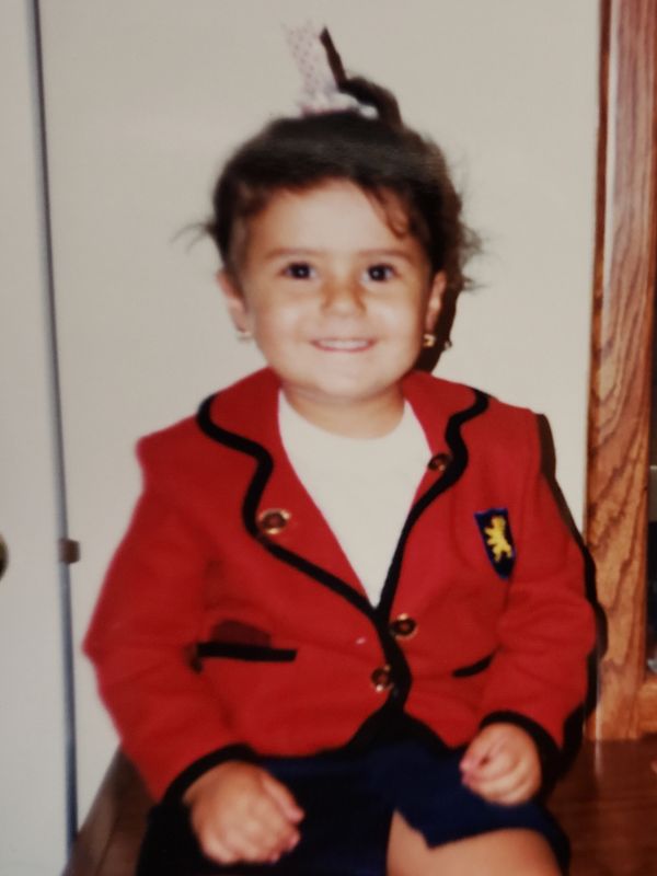 Smiling toddler in red jacket sitting indoors.