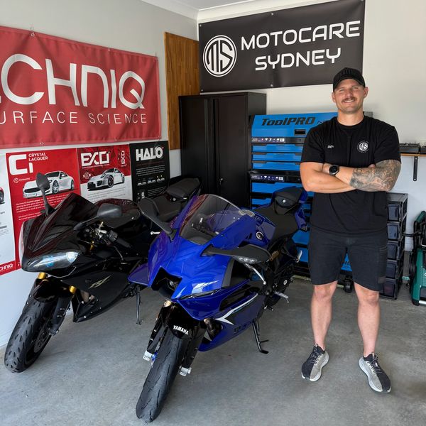 Man standing next to two sport motorcycles in a garage with banners behind.