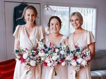 Three women in matching dresses holding colorful bouquets, smiling.