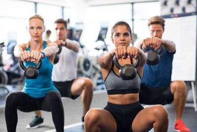 Four people kettlebell squatting.