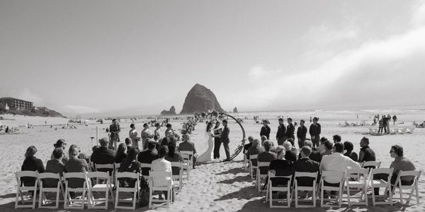 Black and white beach wedding with guests seated and couple under circular arch.