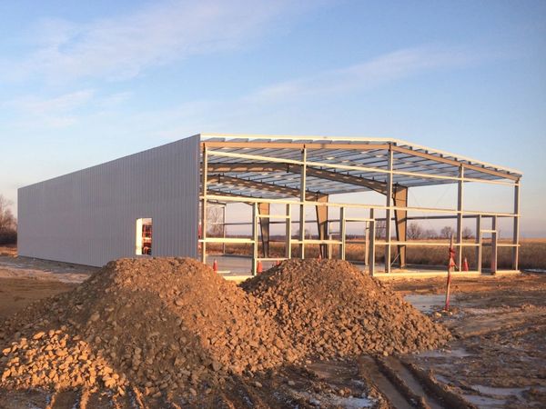 A photograph of a pre-engineered metal building under construction at sunrise.