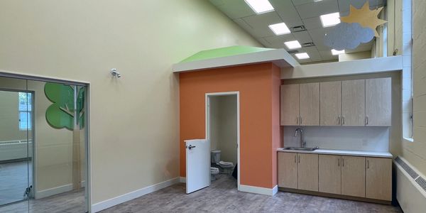 An activity room with millwork countertop, toddler washroom access, and glass panels at corridor.