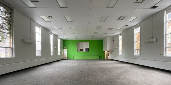 Interior photo of the existing community hall with tall side windows and plenty of daylight.