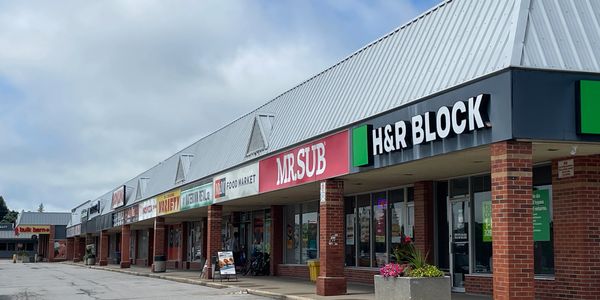 Photo of the existing retail plaza with low canopy roof and non-uniform signs.