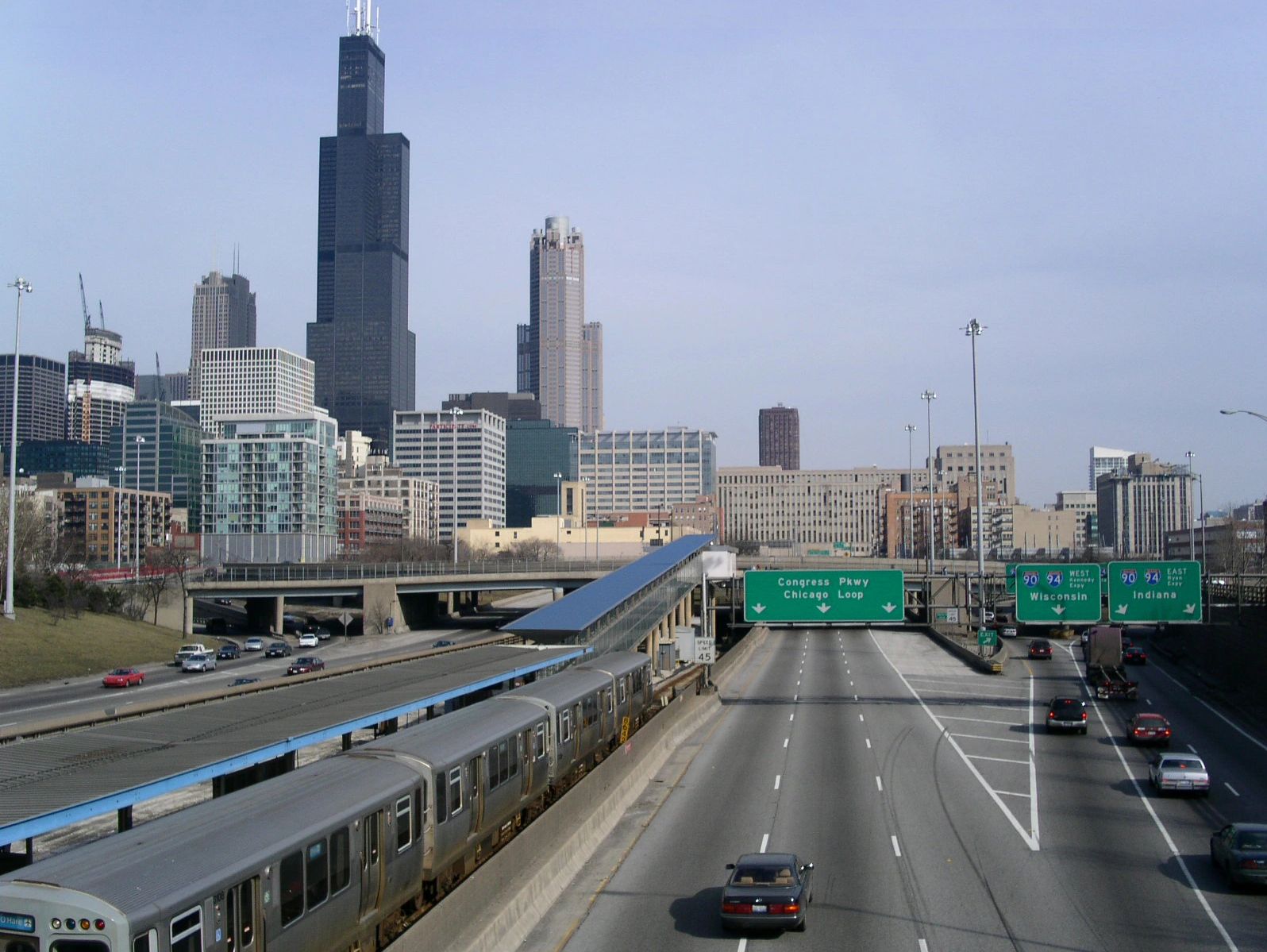 The Chicago skyline with a train, highway, and green road signs ahead that reads, "Chicago Loop".